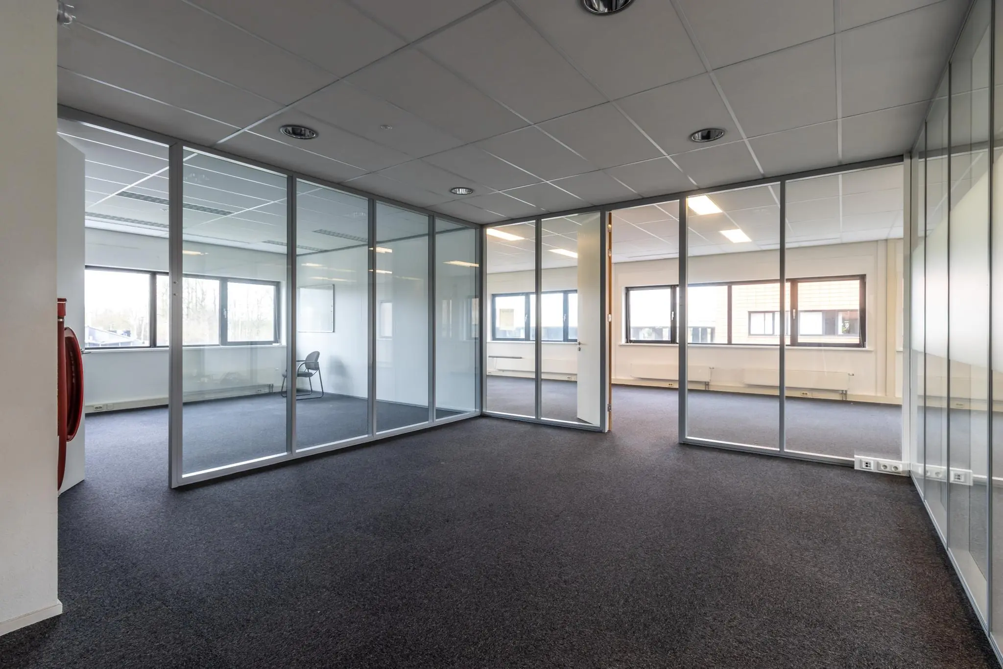 Leeg kantoorpand aan de Lage Biezenweg met glazen scheidingswanden en uitzicht op buiten.